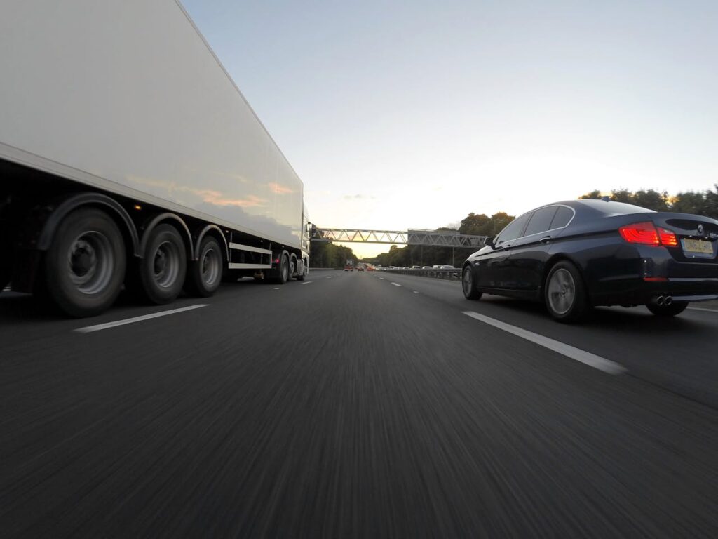 Blue Infiniti Sedan Running on Road Togerther With White Freight Truck